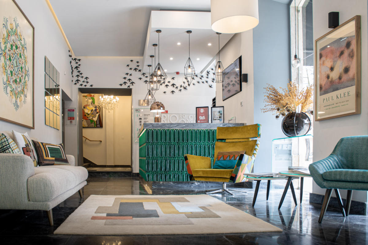 Moderna hall dell'hotel Rio Art, Setúbal, con arredi contemporanei, decorazioni geometriche, luci sospese e opere d'arte alle pareti; sullo sfondo il banco della reception.