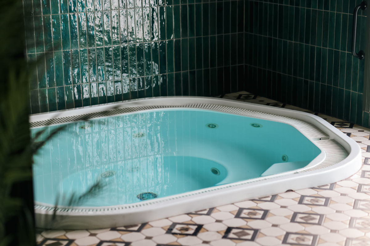 Una piccola vasca idromassaggio interna con acqua limpida, bordo bianco e pareti piastrellate verdi, situata su un pavimento di piastrelle a motivi.