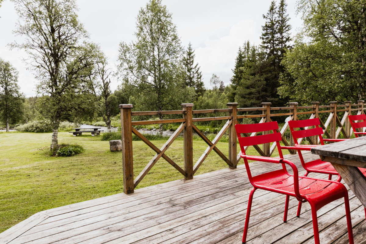 Des chaises rouges et une table en bois sont installées sur une terrasse donnant sur une zone herbeuse avec des arbres, une clôture et une table de pique-nique en arrière-plan au Storsätra Mountain Hotel.