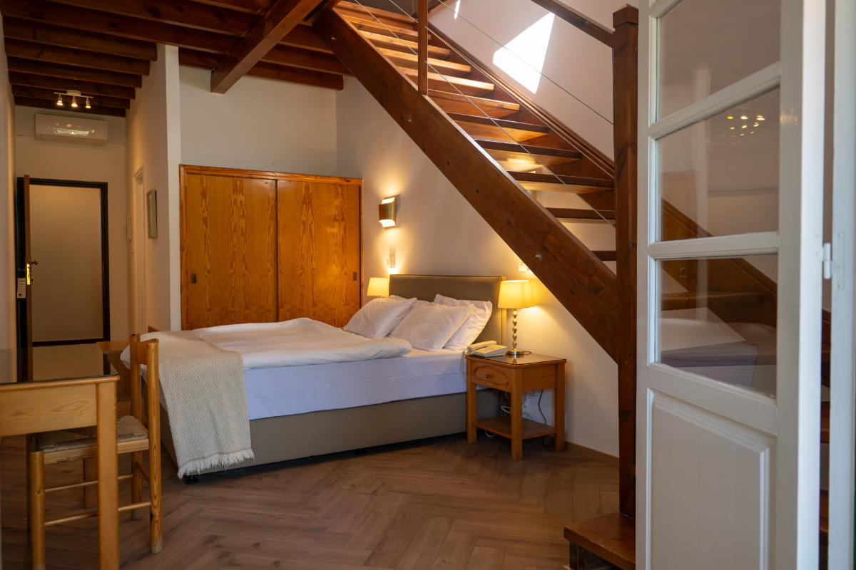Une chambre confortable avec un lit double, des meubles en bois, une lampe de chevet et un escalier menant à un niveau supérieur.