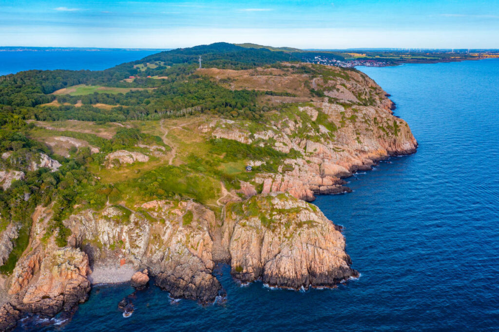 Secret shores: Europe’s best coastal towns for late summer 8 Aerial view of a rocky coastline with cliffs, green vegetation, and blue ocean under a clear sky—an inviting glimpse of coastal towns for late summer escapes.