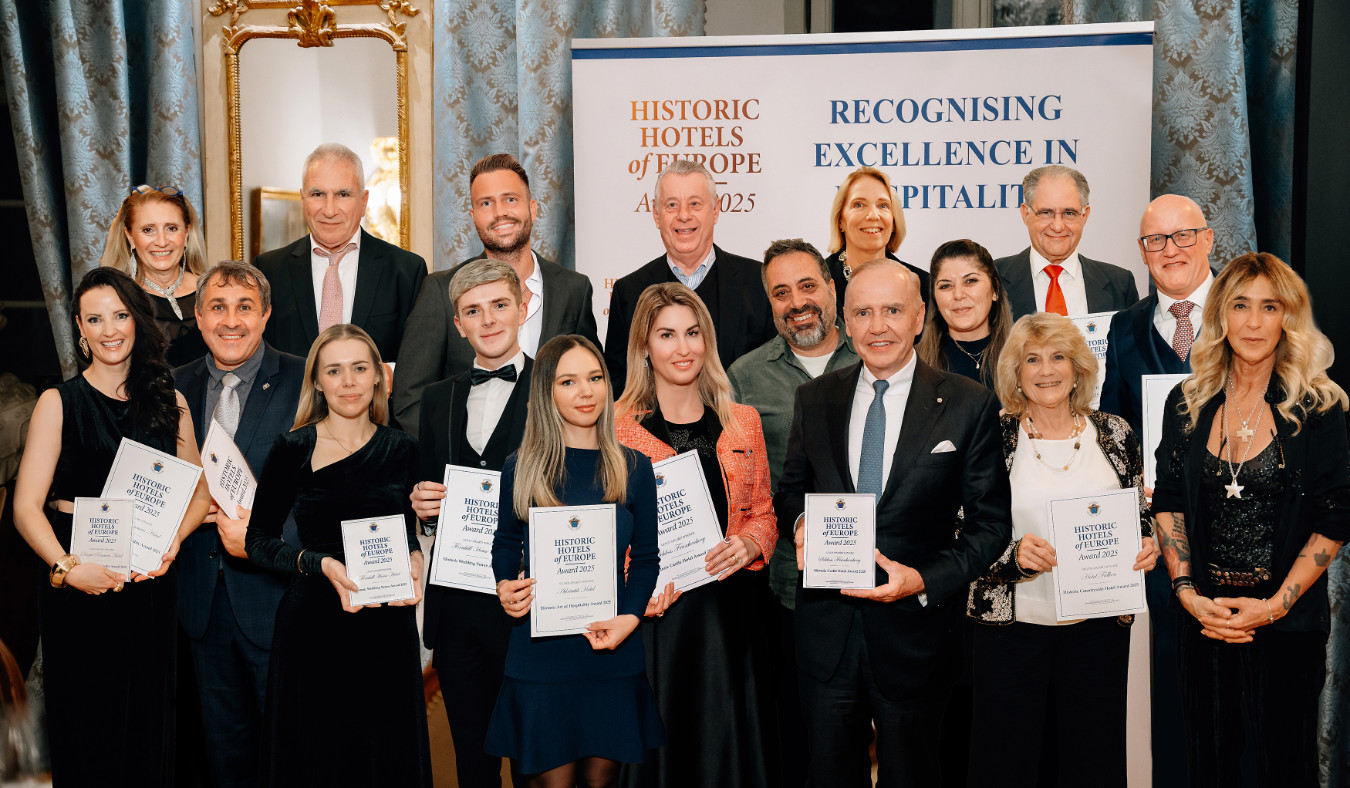 A group of people pose indoors, some holding certificates, in front of banners reading "Historic Hotels of Europe" and "Recognising Excellence in Hospitality," celebrating the Historic Hotels of Europe Awards 2025.