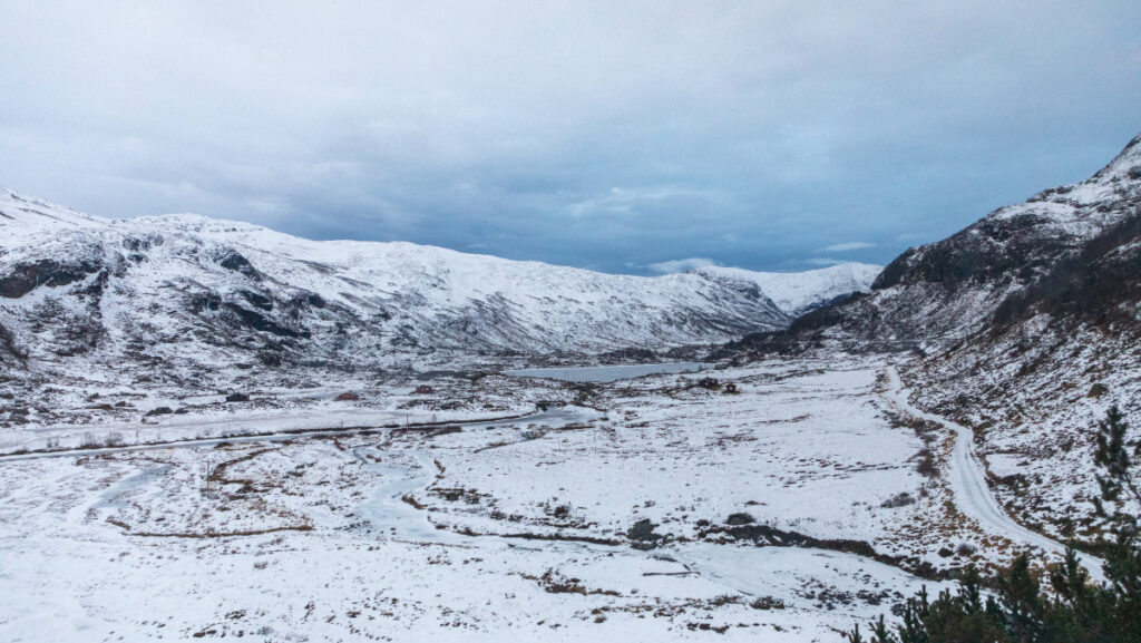 Viajes de invierno en tren: hoteles históricos en las rutas ferroviarias europeas 5 Valle nevado rodeado de montañas bajo un cielo nublado, con un río serpenteando por el paisaje y la carretera Bergenline visible a la derecha.
