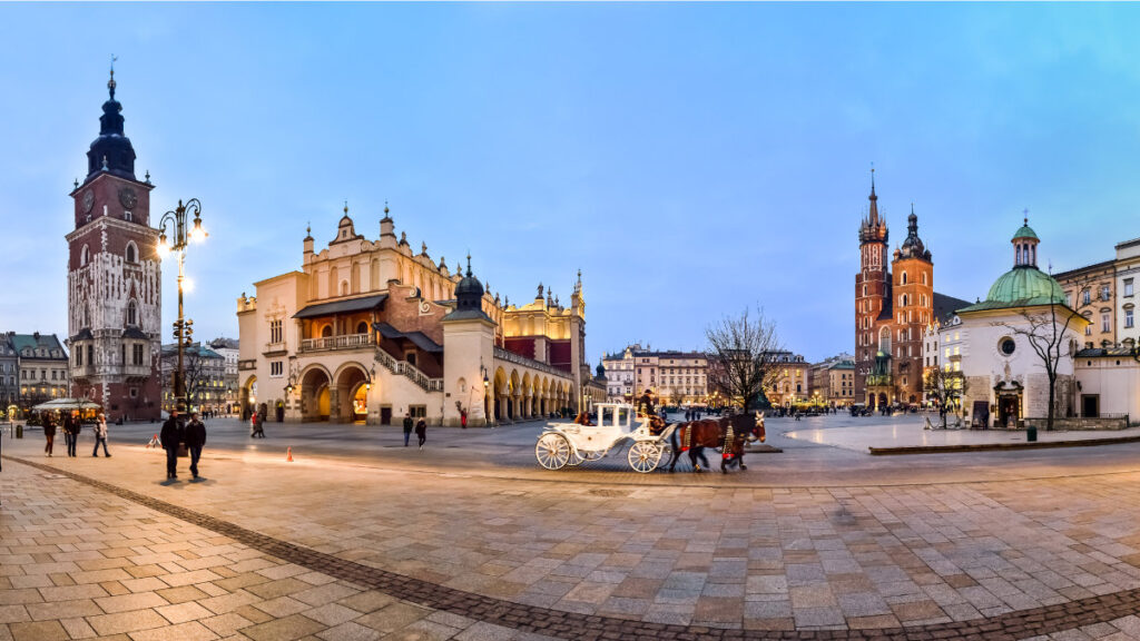 My Town : Kraków - Guide de la ville 2 Une vue panoramique de la place de Cracovie avec des bâtiments historiques, une tour d'horloge, une église, des gens qui marchent et une calèche blanche - une scène parfaite de tout guide de la ville de Cracovie.