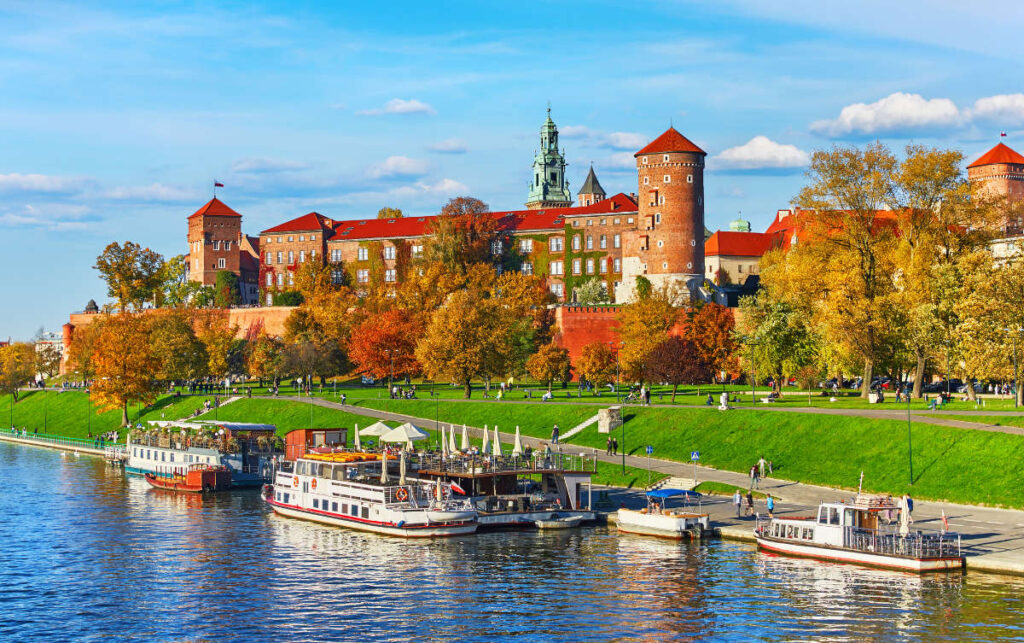 My Town : Kraków - City guide 6 Vue du château de Wawel à Cracovie, en Pologne, avec des bateaux d'excursion amarrés le long de l'eau et des gens qui se promènent par une journée d'automne ensoleillée - une scène parfaite qui figure dans tout guide de la ville de Cracovie.