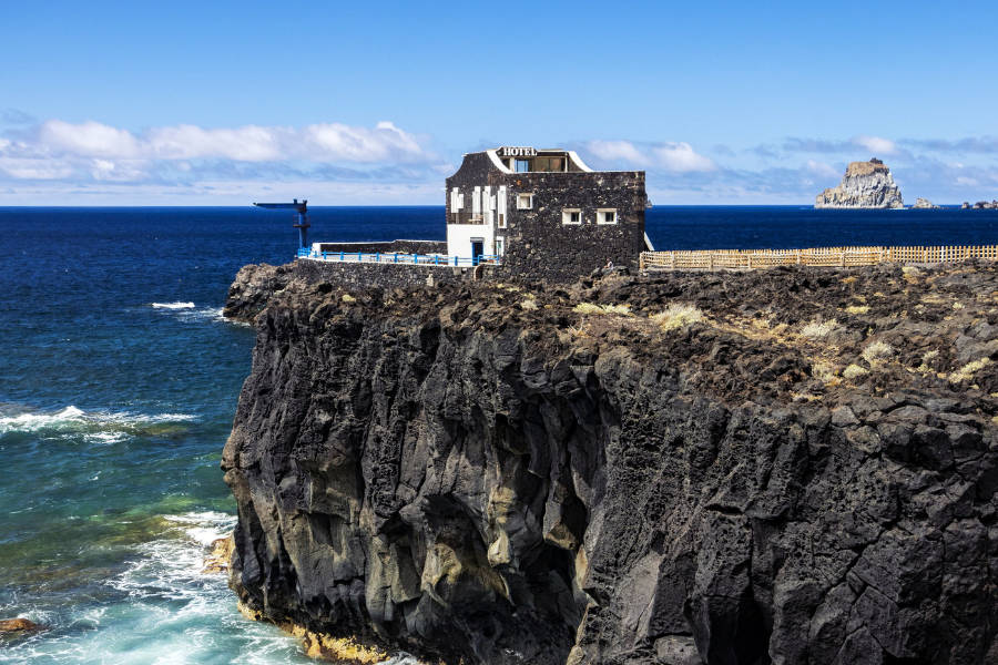 I 20 hotel più romantici d'Europa 14 Un piccolo edificio in pietra si trova sul bordo di una scogliera rocciosa sopra l'oceano, sotto un cielo azzurro e limpido con isole lontane visibili: è l'Hotel Puntagrande.