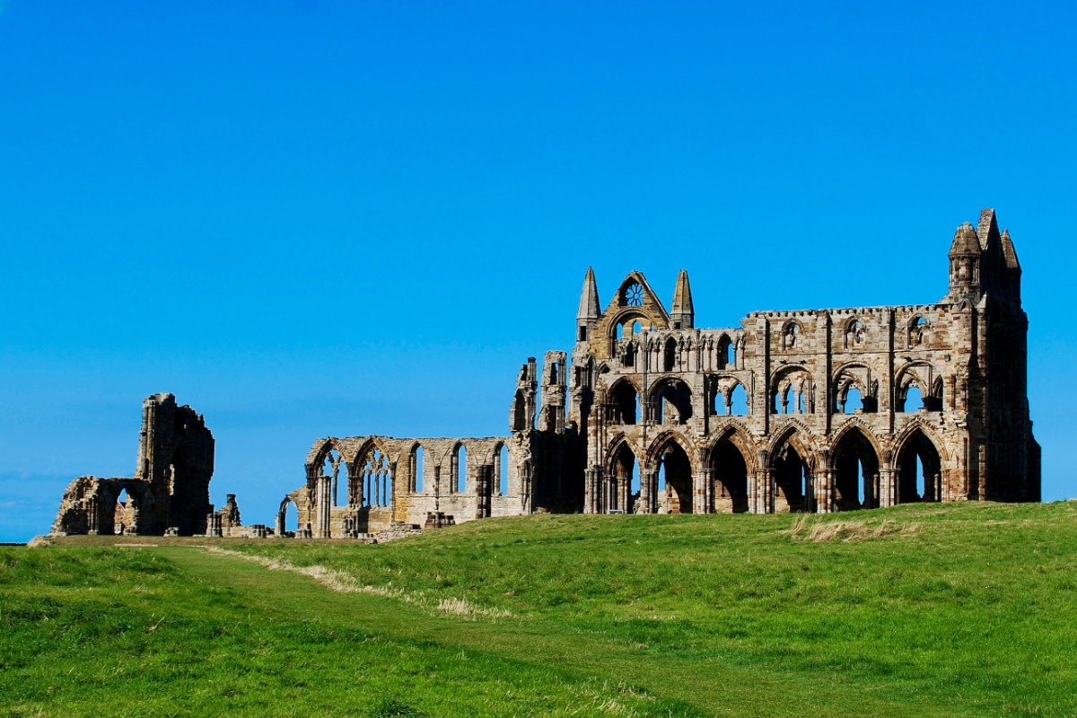 Ruinen der Abtei von Whitby mit gewölbten Fenstern und Mauern stehen auf einem grasbewachsenen Hügel in England
