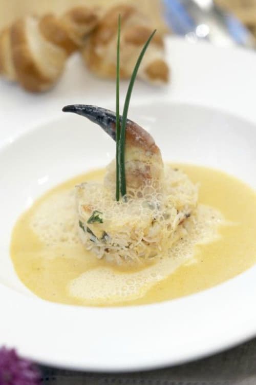 At Dunbrody House Hotel, a crab claw is served upright in a round seafood mousse with creamy sauce and foam, garnished with two chives, on a white plate with bread in the background—a true 4 star hotel Ireland experience.