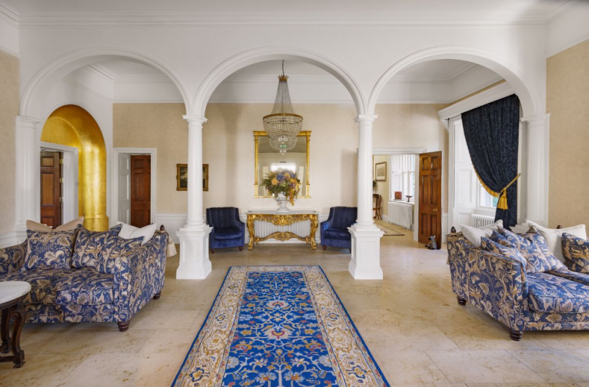 Salon élégant de l'hôtel Dunbrody House avec des portes cintrées, des canapés bleus à motifs, un tapis bleu et or, un lustre et une console dorée avec une composition florale sous un grand miroir - un vrai charme d'hôtel 4 étoiles en Irlande.