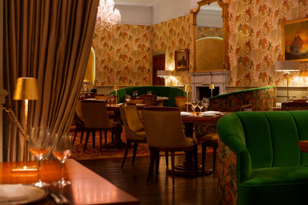 L'élégante salle à manger du restaurant de l'hôtel Dunbrody House avec son papier peint fleuri, ses canapés en velours vert, ses tables en bois, ses chaises rembourrées, son lustre et ses grands miroirs ornés - une véritable expérience d'hôtel 4 étoiles en Irlande.