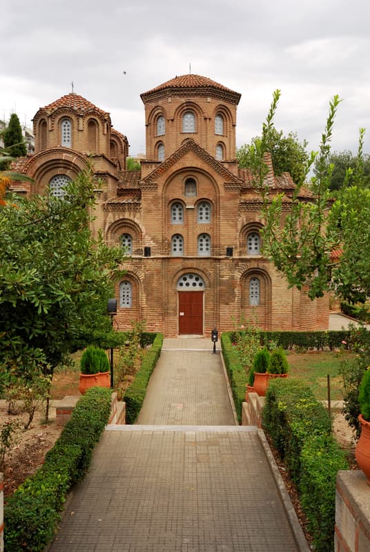 Belle come un quadro: cinque destinazioni europee che ispirano gli artisti 11 Una chiesa in stile bizantino con pareti in mattoni, finestre ad arco e cupole ricoperte di tegole rosse, circondata da un sentiero che attraversa il giardino e dal verde.