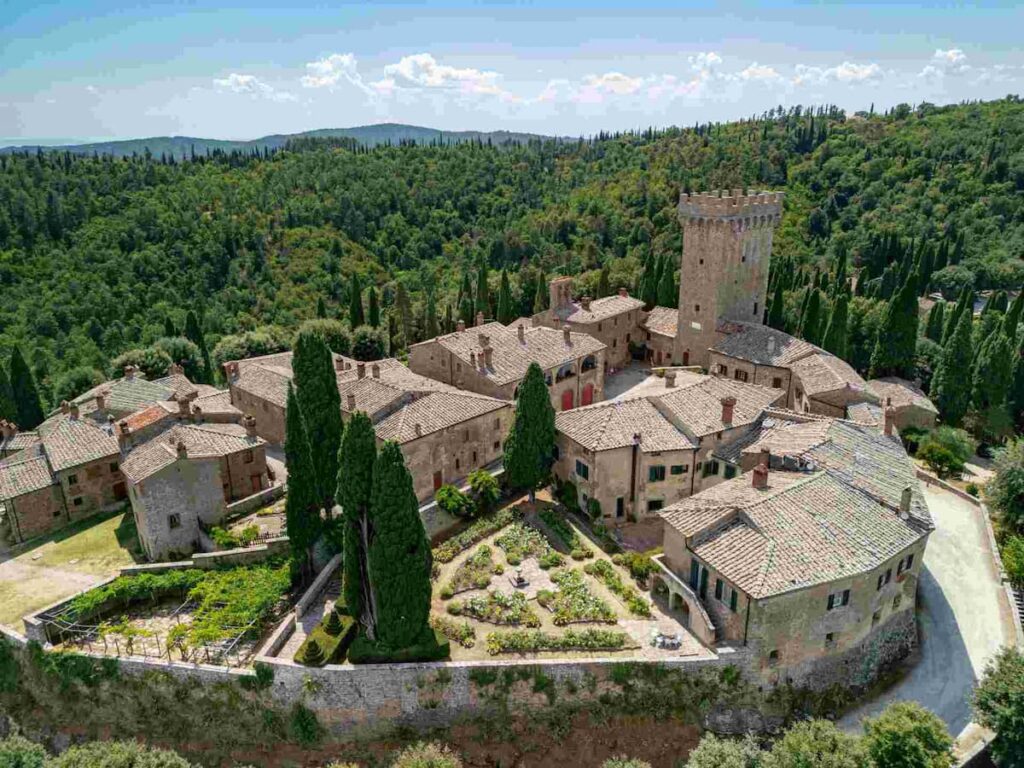 Belle come un quadro: cinque destinazioni europee che ispirano gli artisti 7 Vista aerea del borgo medievale in pietra di Castello di Gargonza, in Toscana, Italia, circondato da alberi e colline sotto un cielo sereno.