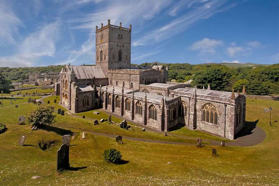 Belle come un quadro: cinque destinazioni europee che ispirano gli artisti 5 Una vecchia cattedrale in pietra sorge in mezzo a un cimitero erboso costellato di lapidi, sotto un cielo azzurro solcato da nuvole sottili.