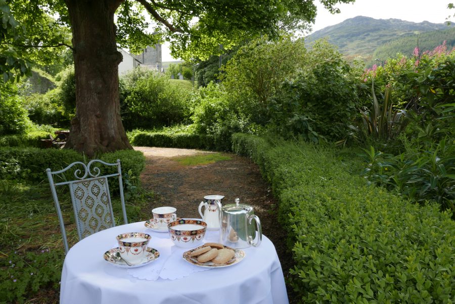 Une table blanche, sur laquelle sont disposés un service à thé et des biscuits, se trouve dans le jardin de Ghan House, en Irlande.