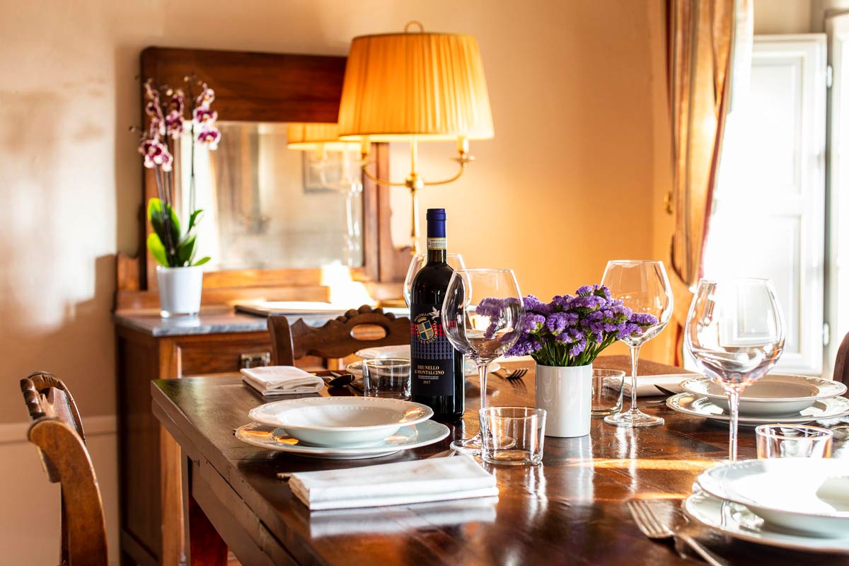 A dining table set with white plates, wine glasses, and a bottle of Brunello di Montalcino wine at Palazzo Tiglio, Tuscany, Italy